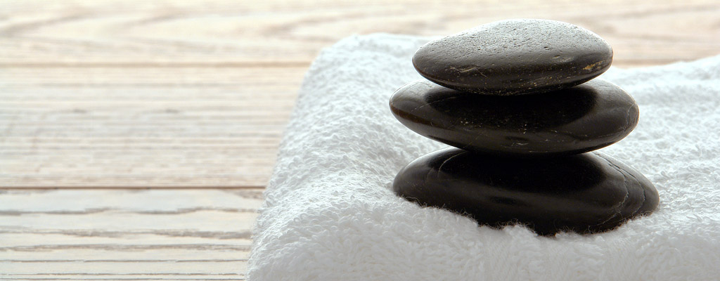 A fresh white towel and a stack of polished massage stones sit on a weathered table top.